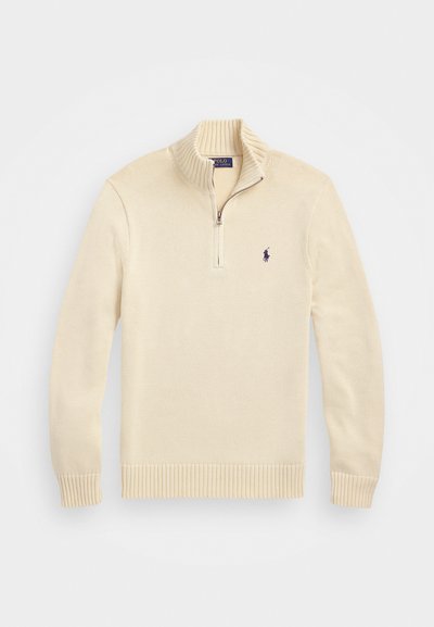 Pull en tricot couleur crème avec une fermeture éclair à quart de longueur, des bords-côtes aux poignets et à l'ourlet, et un petit logo brodé sur la poitrine gauche.