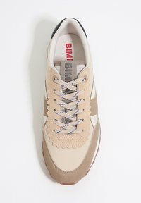 Beige en bruine sneaker met een textuur bovenwerk, zigzagaccenten en blauwe veters. Witte details aan de zijkanten en een rubberen zool.