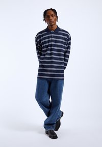 Navy striped polo shirt with white horizontal lines, relaxed fit, paired with wide-leg blue denim jeans and black heeled shoes.
