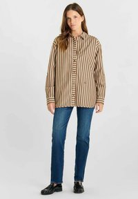 Bruin en witte verticaal gestreepte blouse, relaxte pasvorm met lange mouwen, gecombineerd met blauwe jeans en zwarte instappers.