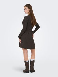 Robe longue à manches longues en maille côtelée marron avec un corsage ajusté et une jupe évasée, associée à des bottes de cowboy marron, avec des chaussettes blanches en accent.