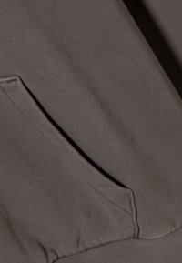 Mørk gråt stoff med en jevn tekstur og en kengurulomme med en subtil ribbestruktur langs kanten. Ingen synlige mønstre eller hardware.