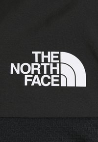 Mustapohjainen kangas, jossa on näkyvä valkoinen "THE NORTH FACE" -logo, joka on muotoiltu kaarevaksi kolmiarkkitehtuuriksi ja jossa on teksturoitu alaosa.