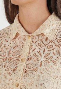 Romantische kanten blouse in crème met bloemmotief, knoopsluiting met kraag en knopen van lichte kleur. Doorzichtige, gestructureerde stofdetails.