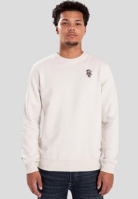 Sudadera de color beige claro, hecha de una tela suave, con un pequeño personaje bordado en el pecho, cuello redondo y puños acanalados.