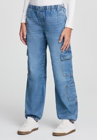 Jasnoniebieskie dżinsowe spodnie cargo z elastycznym pasem, bocznymi kieszeniami i luźnym krojem. Połączone z białymi sneakersami.