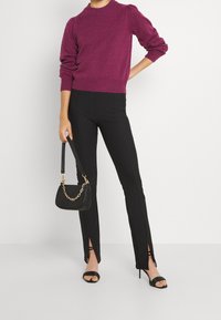 Fuksjowy sweter dzianinowy z bufkami, czarne dopasowane spodnie z bocznymi rozcięciami oraz czarna torebka z łańcuszkiem. Czarne sandały na obcasie.