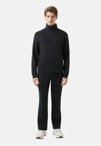 Czarna bluza z zamkiem błyskawicznym i podniesionym kołnierzem oraz dopasowane czarne spodnie. Miękki materiał z minimalnymi zdobieniami i kontrastującymi szwami. W zestawie sneakersy.