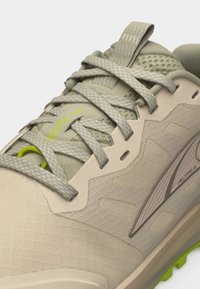 Μπεζ και ανοιχτό πράσινο αθλητικό παπούτσι με υφασμάτινη υφή, λεπτομερείς κορδόνια και λογότυπο της μάρκας στο πλευρό και τη γλώσσα του παπουτσιού.
