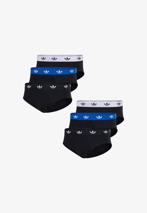 Mężczyzna bez koszulki, ubrany w czarne majtki z czarnym paskiem w talii ozdobionym białymi logo Adidas, pozujący z jedną ręką dotykającą szyi.