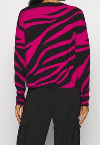 Maglione a righe fucsia e nero con una vestibilità rilassata, maniche lunghe e polsini a costine; presenta un audace motivo zebra sulla schiena.