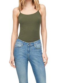 Olijfgroen tanktop met dunne bandjes, gecombineerd met lichtblauwe spijkerbroek met een middelhoge taille en subtiele vervaging langs de benen.
