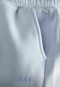 Lysblå joggers lavet af blødt stof, med elastisk talje, sidelommer og et lille broderet logo i blå.