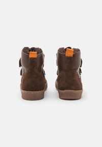 Botines marrones de tobillo con materiales de ante y cuero, que presentan una pestaña de acento naranja, una suela texturizada y un suave forro de felpa en la parte superior.