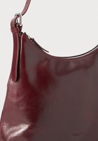 Borsa a spalla in pelle bordeaux con una texture liscia e chiusura con zip argentata. Presenta una singola tracolla per il trasporto. Embossing del logo notevole.