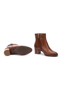 Botas de tobillo de cuero marrón con cremallera lateral, tacón de bloque y suela texturizada, que cuentan con un acabado suave y detalles de costura mínimos.
