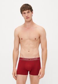 Piros pamut boxer alsónadrág, fehér "TOMMY HILFIGER" logós derékrésszel, amely szoros illeszkedést és sima textúrát kínál.