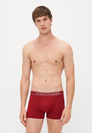 Rote Baumwoll-Boxershorts mit einem weißen „TOMMY HILFIGER“-Logo-Bund, die ein eng anliegendes Design und eine glatte Textur bieten.