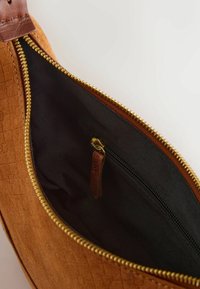 Bolso de cuero marrón con un exterior texturizado, cremallera dorada y un interior de tela negra que cuenta con un pequeño bolsillo con cremallera y una lengüeta de cuero.