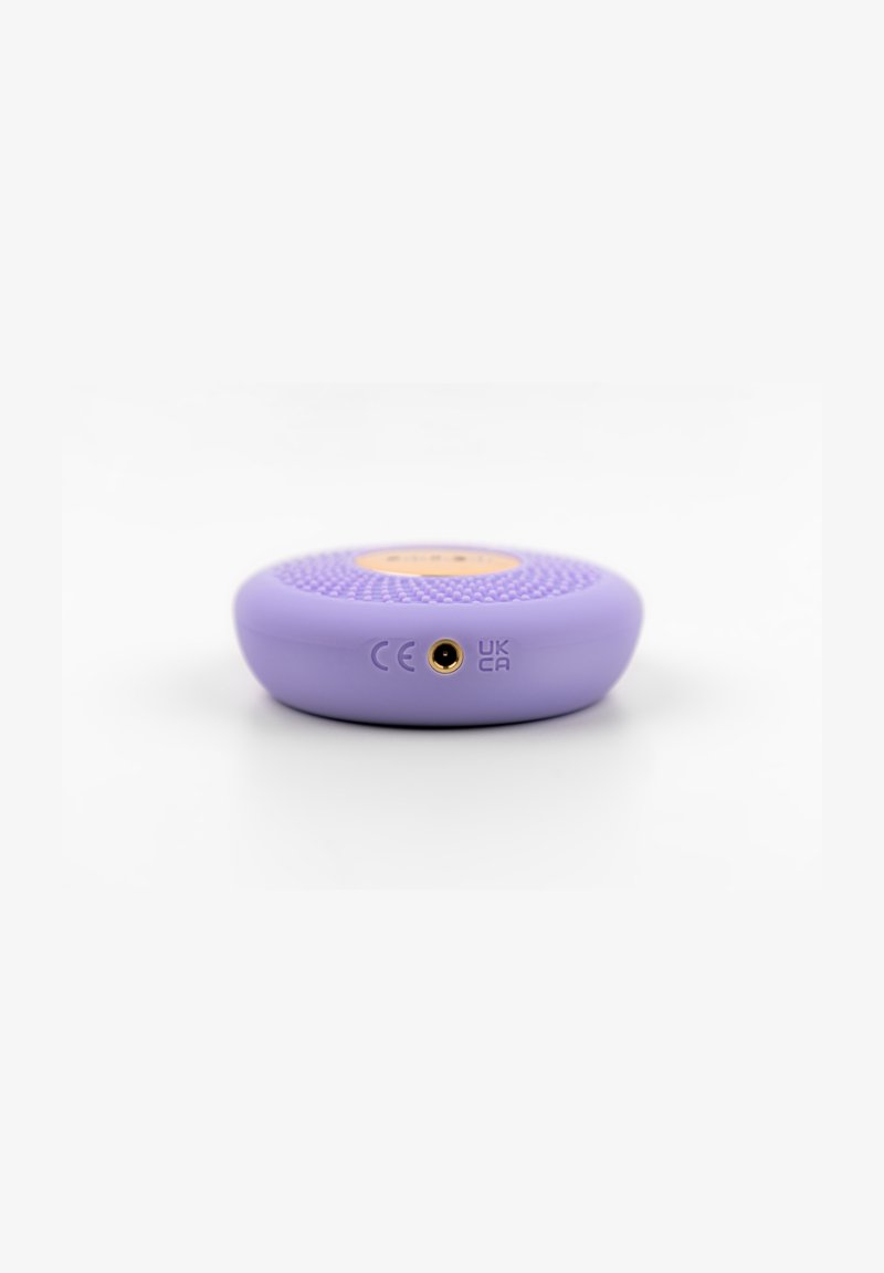 Compact lavender circular speaker with textured top, showing CE and UKCA certification marks and central audio input port on a white background.