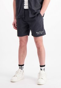 Donkergrijze shorts met een gestructureerd patroon, elastische tailleband en geborduurd logo-detail. Gepaard met witte sportschoenen en contrasterende sokken.