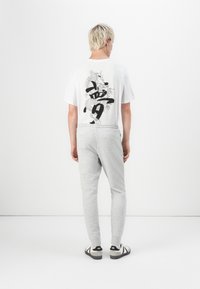 White t-shirt with a black dragon graphic and text on the back, paired with grey sweatpants. The outfit is completed with black and white footwear.