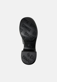 Black rubber shoe sole with embossed "Camper" branding, featuring a rounded shape and a textured surface for grip. Size marked as 38.