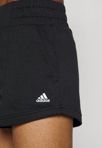 Black athletic shorts with an elastic waistband, side pockets, and a white Adidas logo on the left hem. Soft cotton blend fabric.