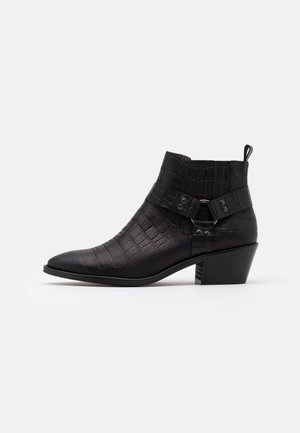 Bottines noires en cuir à motif crocodile texturé, avec un petit talon empilé et des brides décoratives ornées de boucles circulaires.