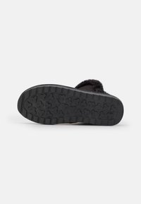 Pantufla de invierno negra con suela gruesa y texturizada y forro suave y esponjoso, mostrada desde la parte inferior sobre un fondo blanco.