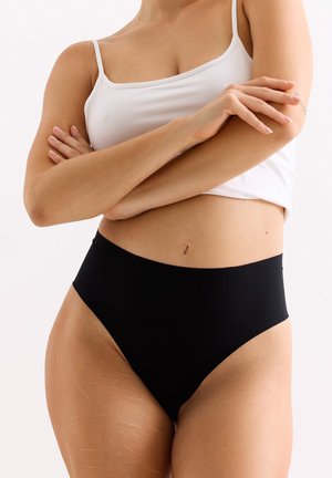 Hoge zwarte broek met een gladde stof, minimale naden en een elastische tailleband. Gecombineerd met een aansluitend wit tanktop.