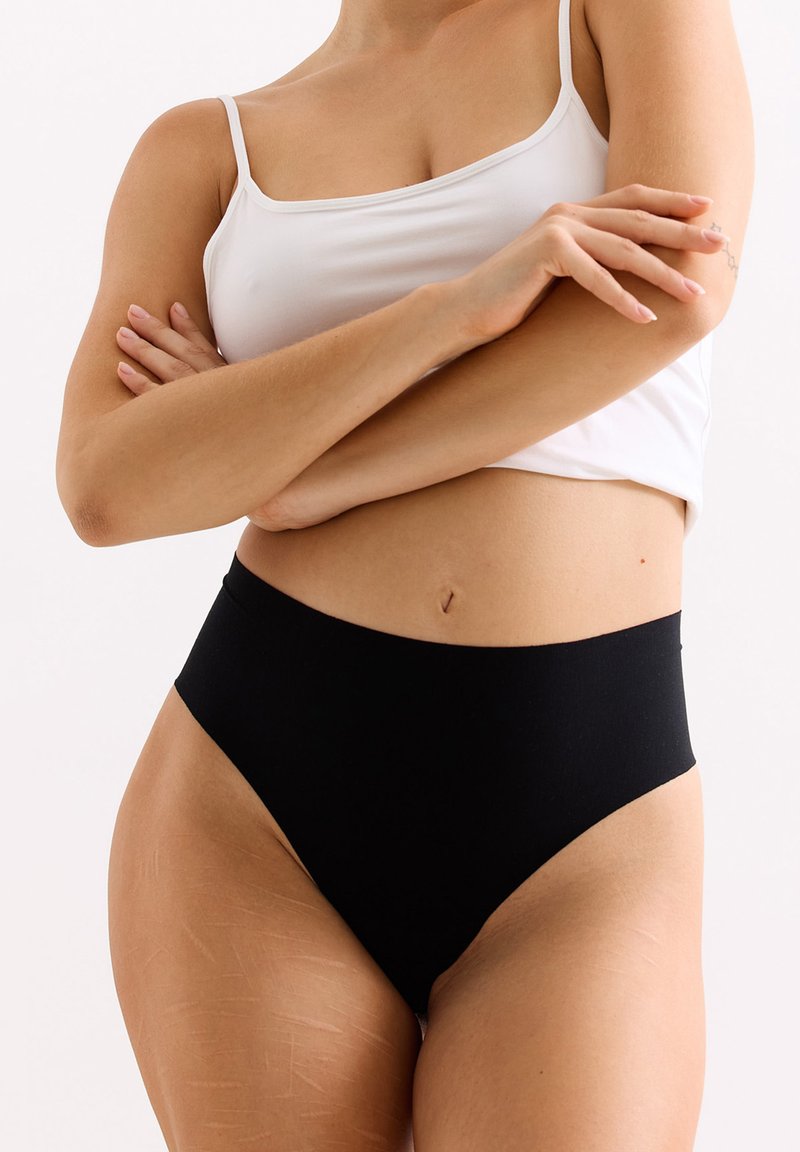 Hoge zwarte broek met een gladde stof, minimale naden en een elastische tailleband. Gecombineerd met een aansluitend wit tanktop.