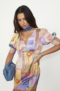 Robe colorée à motifs avec des manches ballons et un décolleté en V profond. Comprend divers motifs floraux abstraits. Un sac à main bleu et un foulard ajoutent une touche de détail.