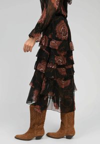 Robe maxi noire à volants avec des motifs floraux rouges et blancs, en tissu transparent, accompagnée de bottes de cowboy marron.
