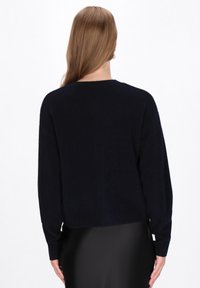 Maglione blu navy in morbido tessuto a maglia con collo rotondo e maniche lunghe, caratterizzato da una vestibilità comoda e polsini e orlo a coste, visto da dietro.