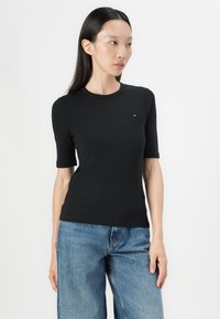 Zwarte ribbed kortek mouwen top met een ronde halslijn en een klein logo detail op de borst, gecombineerd met losse blauwe jeans.