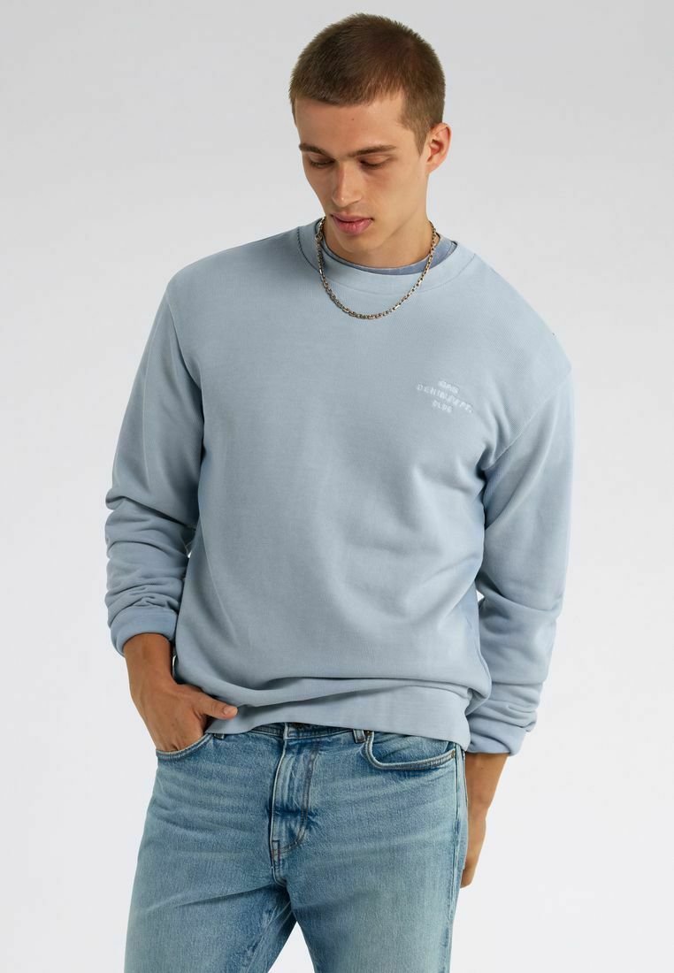 Felpa azzurra chiara con maniche lunghe e colletto a coste. Presenta una piccola grafica sul petto e una vestibilità rilassata. Abbinata a jeans in denim chiaro.