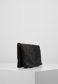 Pochette in pelle nera con superficie testurizzata, caratterizzata da un design a piegatura e sottili dettagli in metallo. Collocata su uno sfondo minimalista.