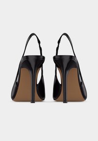 Paire de chaussures à talons hauts slingback en cuir verni noir, vues de dos sur fond blanc.
