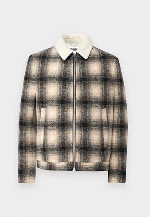 Veste en plaid dans des tons noirs, beiges et crème. Dotée d'un col en fausse fourrure et d'une fermeture éclair intégrale. Tissu doux avec une finition texturée.