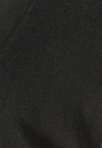 Czarna dzianina pokazana w widoku z bliska, podkreślająca miękką fakturę z subtelnym wzorem i nieregularnymi detalami splotu.