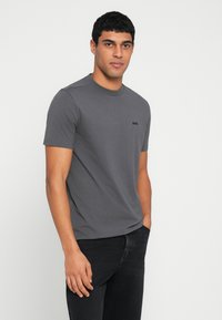 Γκρι κοντομάνικη μπλούζα από μαλακό μείγμα βαμβακιού, με στρογγυλή λαιμόκοψη και διακριτικό μαύρο λογότυπο στο στήθος. Συνδυασμένη με μαύρο τζιν.