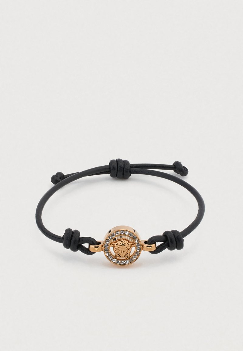 Juodas odinis apyrankė su reguliuojamais mazgais, puošta auksine apvalia medalionu su liūto galvos dizainu, apsupta skaidrių cirkonio akmenėlių.