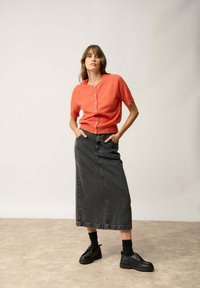 Korallfärgad kortärmad cardigan med knappar, ihop med en lång, mörk denimkjol och svarta plattformsskor. Slät tyg och strukturerad passform.