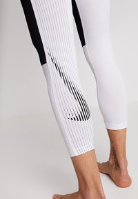 White leggings with black accents, featuring vertical lines and a sleek design. Made from stretchy material for active wear.