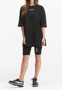T-shirt nera oversize con maniche corte, con un logo bianco. Pantaloni da ciclismo neri e sneakers nere con dettagli bianchi.