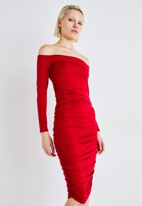 Rochie roșie cu umerii descoperiți, cu mâneci lungi, având detalii de pliu pe laterale și o siluetă ajustată. Material neted și elastic.