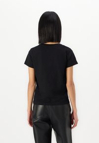 Μαύρη βαμβακερή μπλούζα με κοντά μανίκια και στρογγυλή λαιμόκοψη, με στενή εφαρμογή και απλό σχέδιο. Η πίσω πλευρά δεν έχει γραφικά.