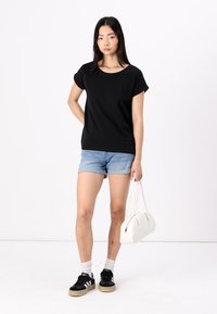 T-shirt noir à manches courtes ; short en denim bleu clair ; sac à main blanc ; baskets noires avec des accents blancs et des semelles grises ; chaussettes blanches.