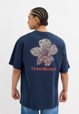Camiseta de algodón azul marino con un gran diseño de flor de mosaico en blanco y rojo en la parte posterior, con la palabra "Teselación" debajo.